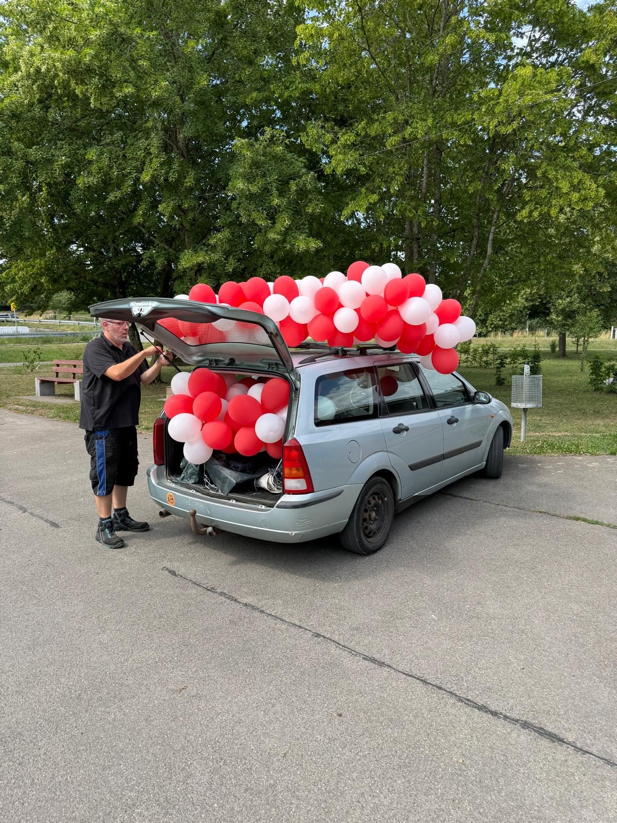 Kombi voller rot-weißer Luftballons, ein Helfer öffnet die Heckklappe
