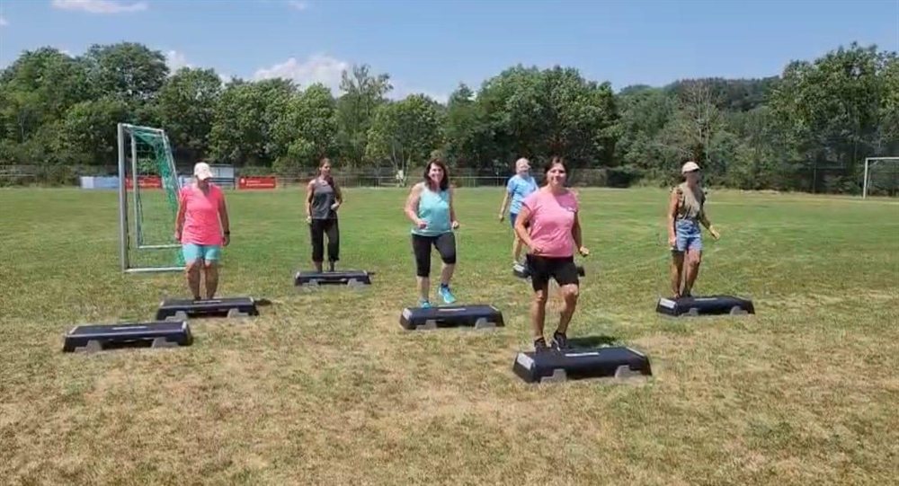Die Fitnessdamen beim Training mit Steppern auf dem Rasen des Sportplatzes