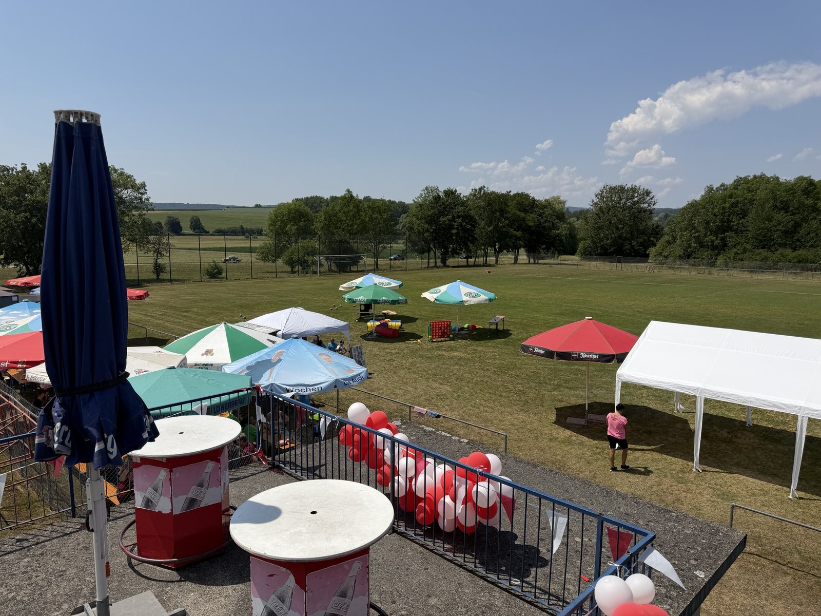 Blick von der Terrasse auf den Sportplatz mit Sonnenschirmen, Festzelt und rot-weißen Luftballons