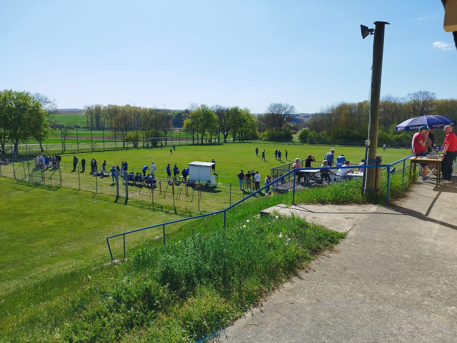 Blick von der Terrasse auf den Sportplatz mit Spielern und Zuschauern