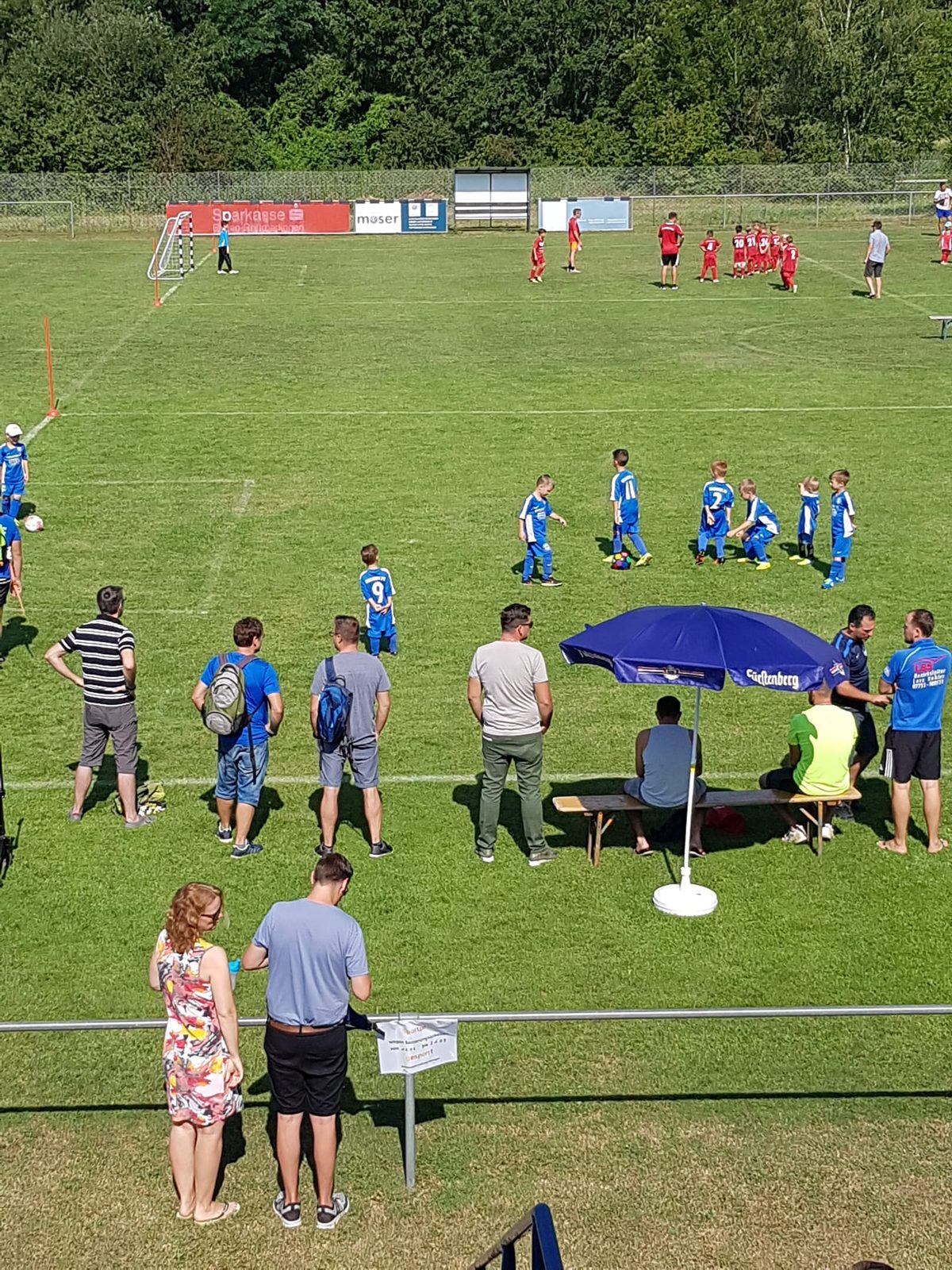 Kinder spielen auf dem Rasen, Eltern und Trainer schauen zu