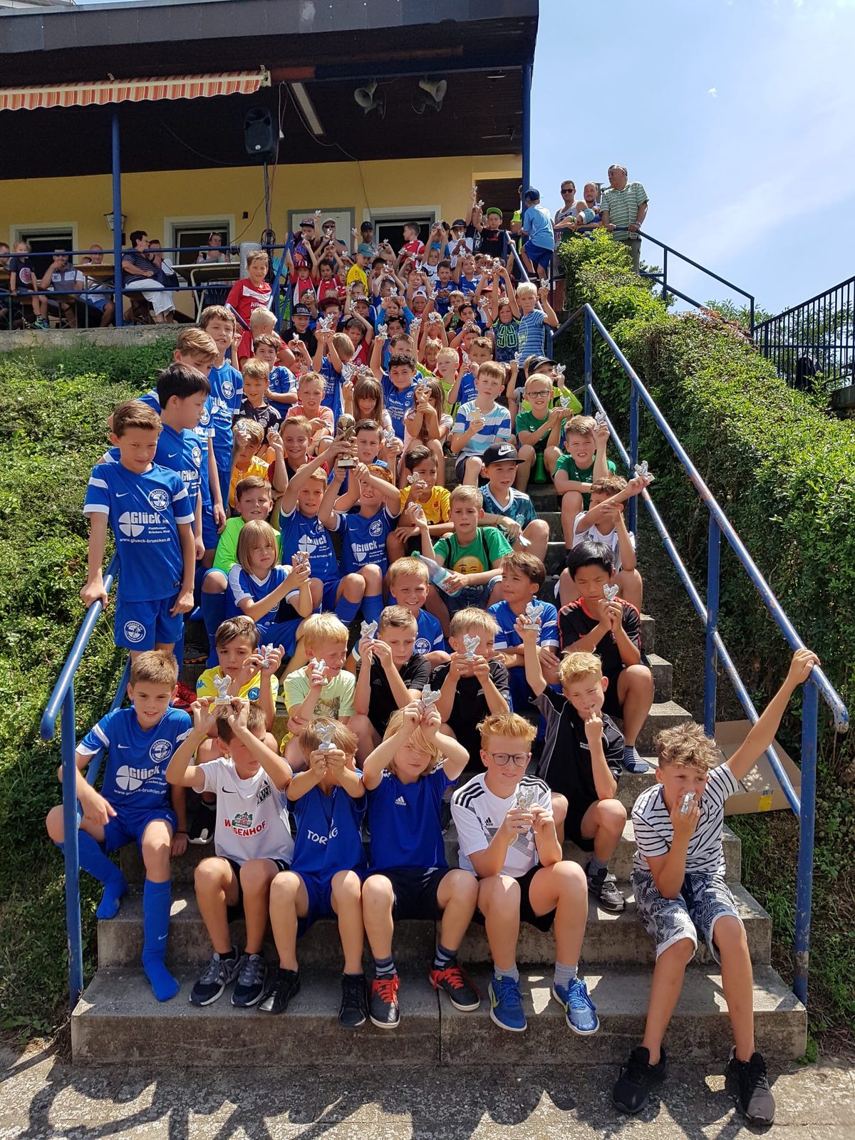Kinder mit kleinen Pokalen auf der Treppe am Sportheim